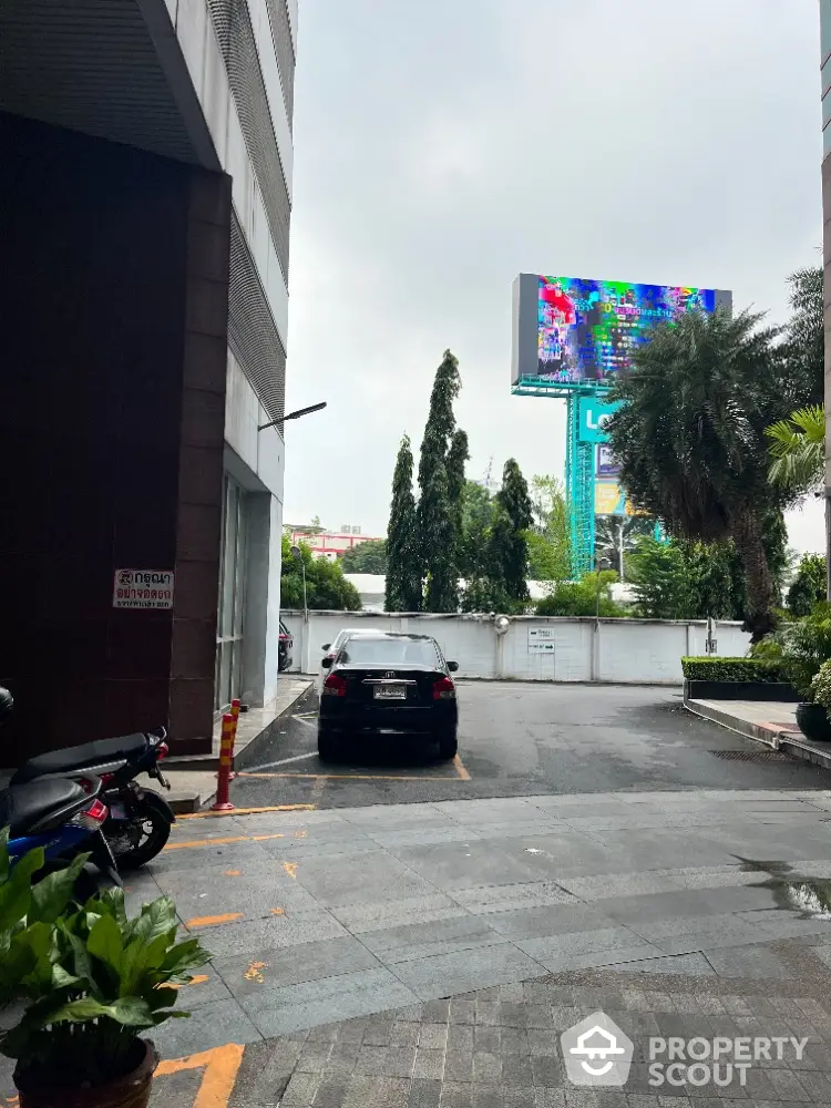 Modern urban building entrance with parking area and lush greenery.