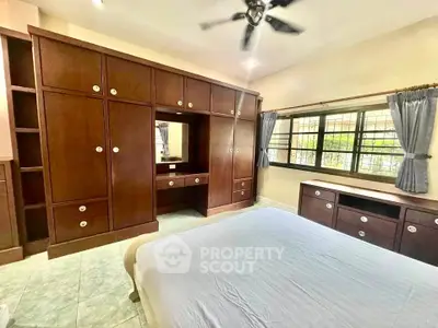 Spacious bedroom with built-in wooden wardrobes and large window for natural light.