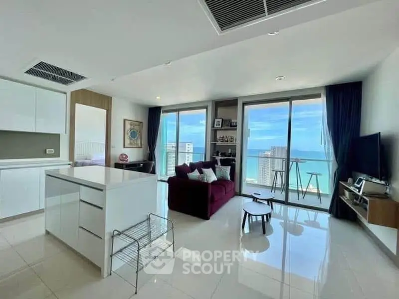 Modern open-plan living room with ocean view, featuring sleek kitchen island and cozy seating area.