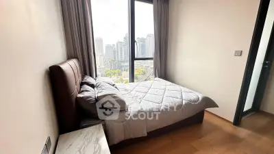 Modern bedroom with city view, featuring a cozy bed and large window in a high-rise apartment.