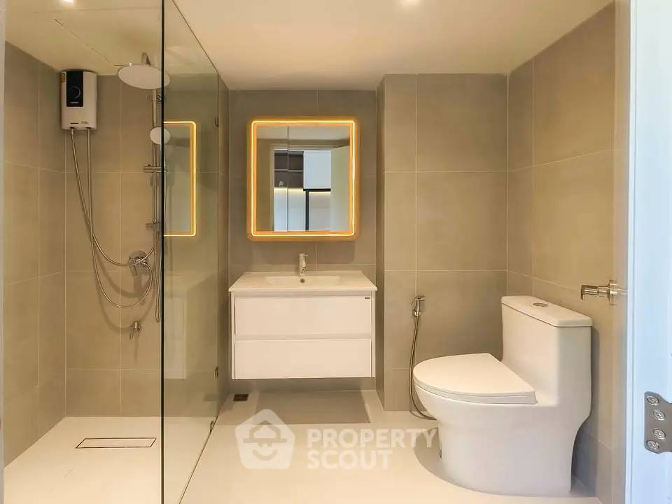 Modern bathroom with glass shower and illuminated mirror in a sleek design.