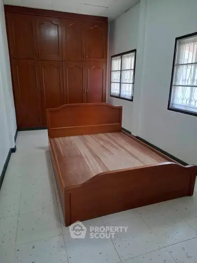 Spacious bedroom with wooden bed and built-in wardrobe, natural light from two windows.