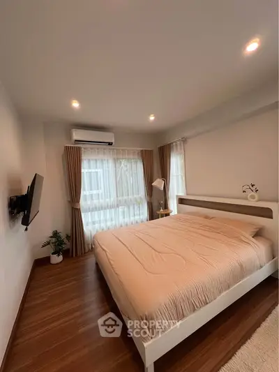 Modern bedroom with cozy decor and natural light, featuring a mounted TV and stylish curtains.