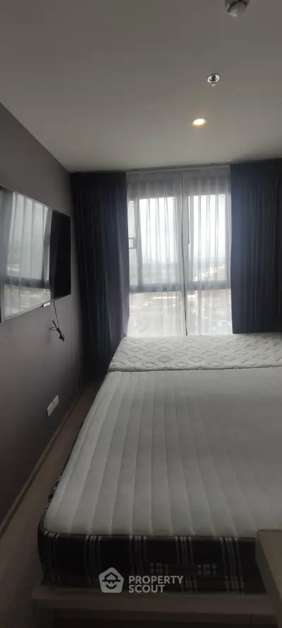 Modern bedroom with large window and wall-mounted TV in a stylish apartment.