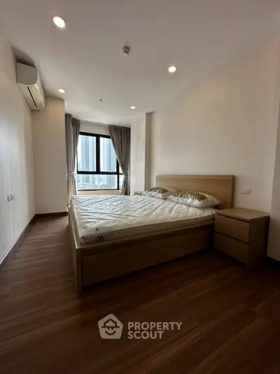 Spacious bedroom with wooden flooring and large window offering city views.
