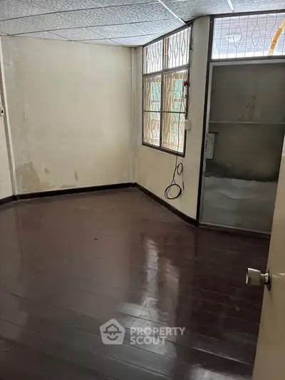 Spacious empty room with wooden flooring and large window, ideal for customization.