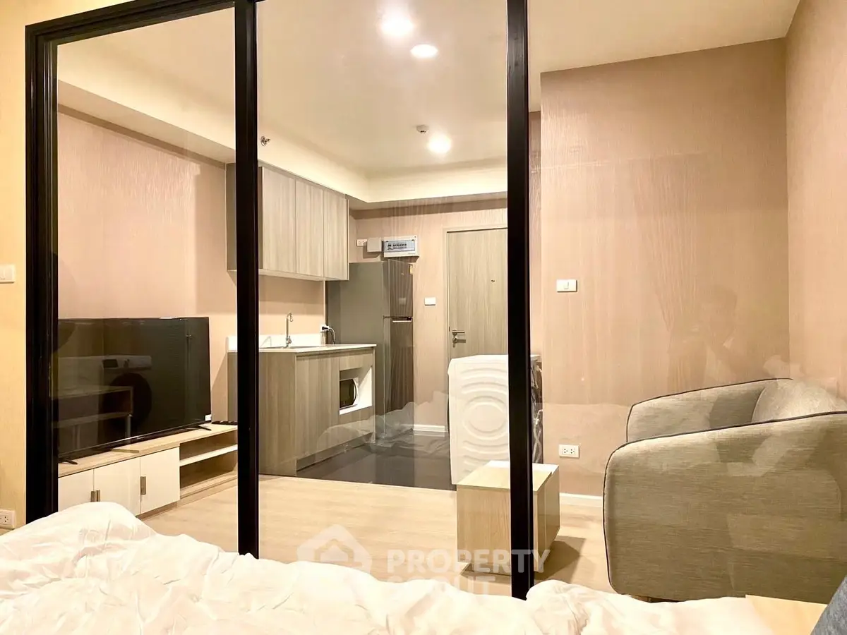 Modern studio apartment with glass partition, cozy living area, and compact kitchen.
