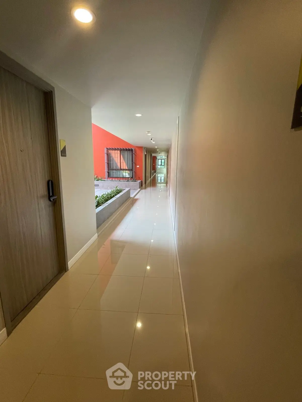 Modern apartment hallway with glossy tiled floors and vibrant red accent wall.