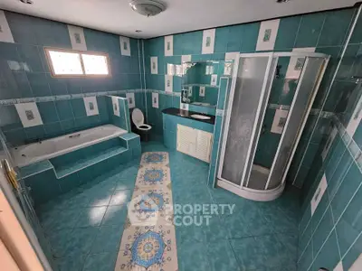 Spacious turquoise-tiled bathroom with bathtub and shower enclosure, perfect for relaxation.