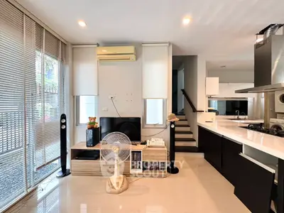Modern living room with sleek kitchen, stylish decor, and natural light from large windows.