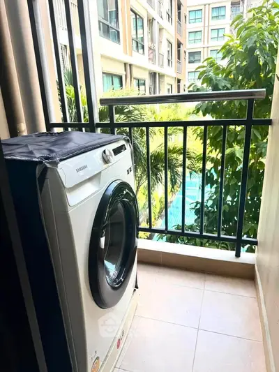 Charming balcony with washing machine overlooking lush greenery and pool view in modern apartment complex.