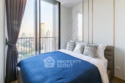 Modern bedroom with large windows and city view, featuring elegant decor and cozy bedding.