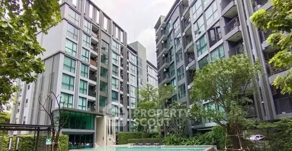 Modern condominium complex with lush greenery and inviting swimming pool.