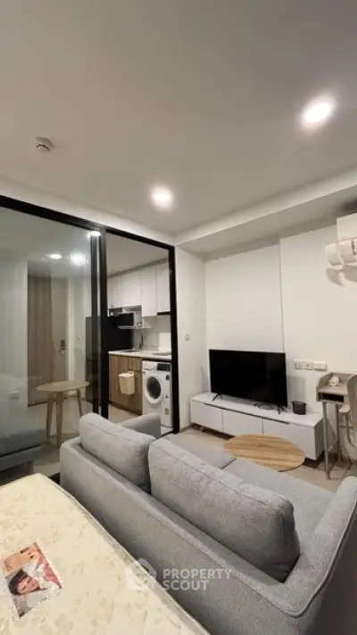 Modern living room with open kitchen and washing machine, featuring sleek furniture and ambient lighting.