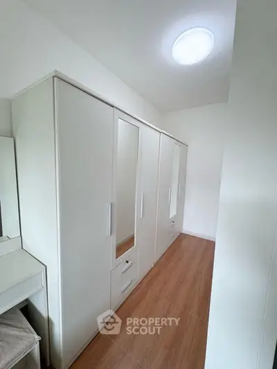 Spacious walk-in closet with modern white wardrobes and wooden flooring.
