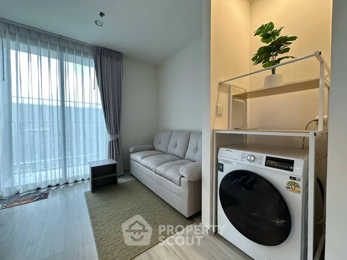 Modern living room with cozy sofa and in-unit washing machine, featuring natural light and stylish decor.
