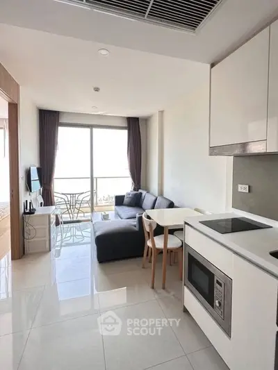Modern living room with open kitchen and balcony view, featuring sleek furniture and natural light.