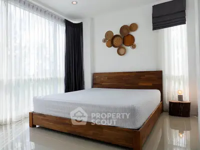 Modern bedroom with wooden bed frame and stylish wall decor, featuring large windows for natural light.