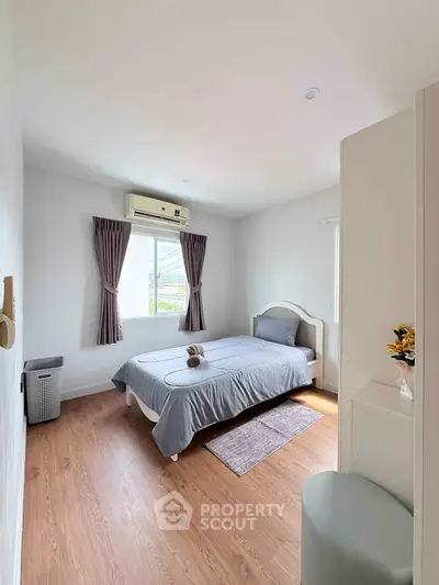 Cozy bedroom with wooden flooring, air conditioning, and natural light from window.