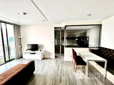 Modern open-plan living room with kitchen, featuring sleek furniture and large windows for natural light.