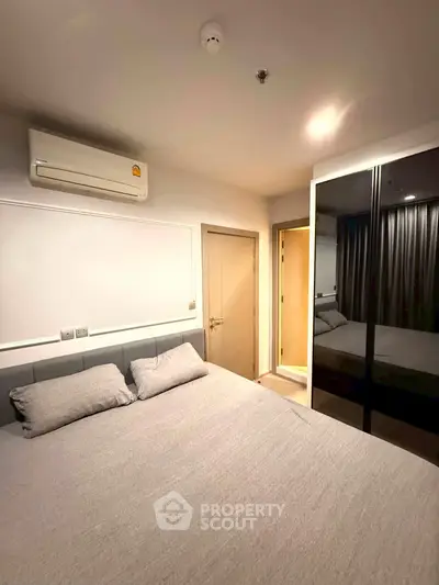 Modern bedroom with sleek design, featuring a comfortable bed, mirrored wardrobe, and air conditioning unit.