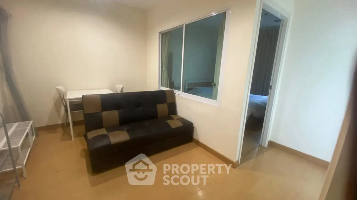 Cozy small living room with sofa and desk, adjacent to a bedroom.