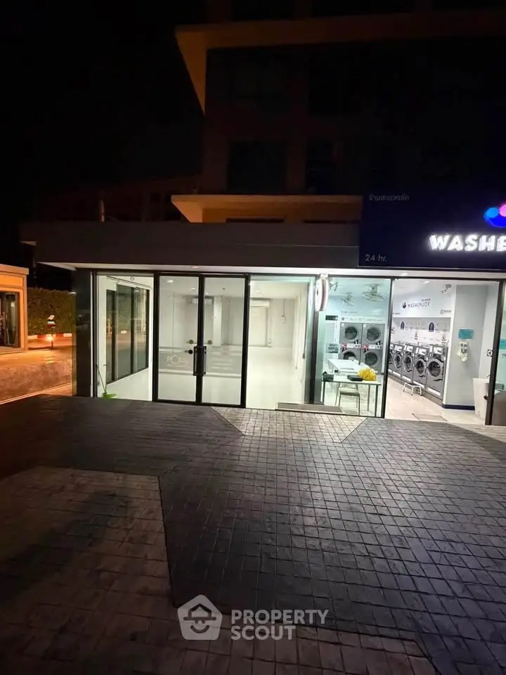 Modern laundromat exterior with glass doors and bright interior lighting at night.