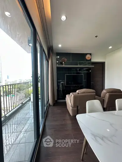 Modern living room with large windows and balcony view, featuring stylish furniture and sleek design.