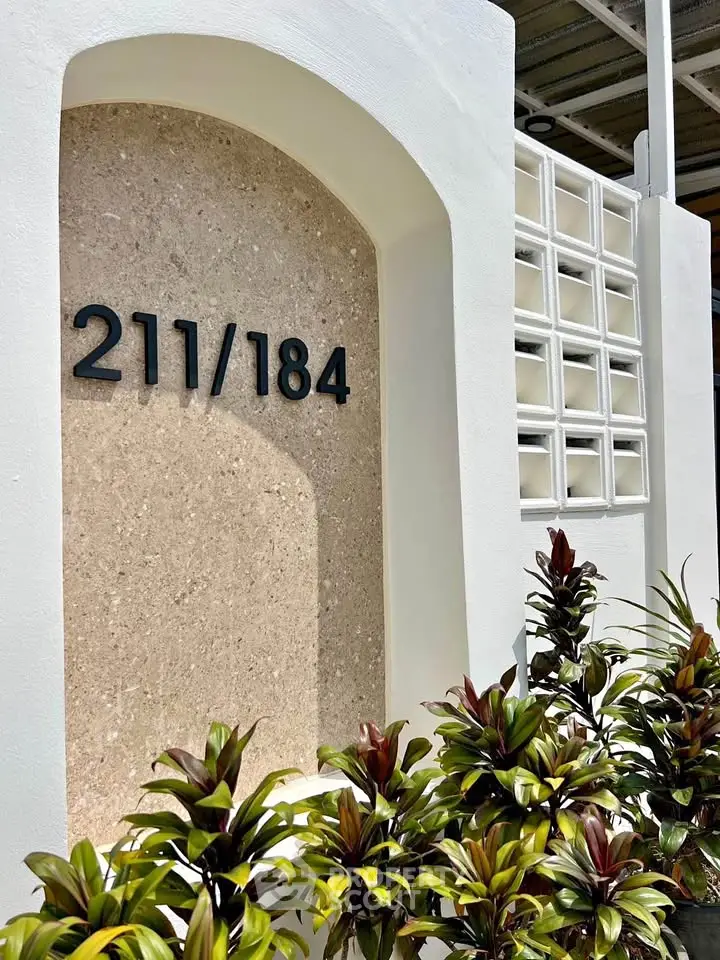 Modern building entrance with unique architectural design and lush greenery, showcasing property number 211/184.