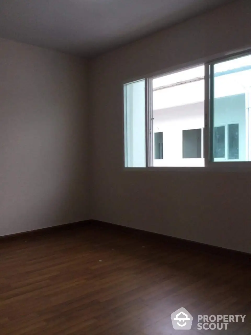 Spacious, unfurnished room with polished hardwood flooring and ample natural light from large windows, ready for personalization.