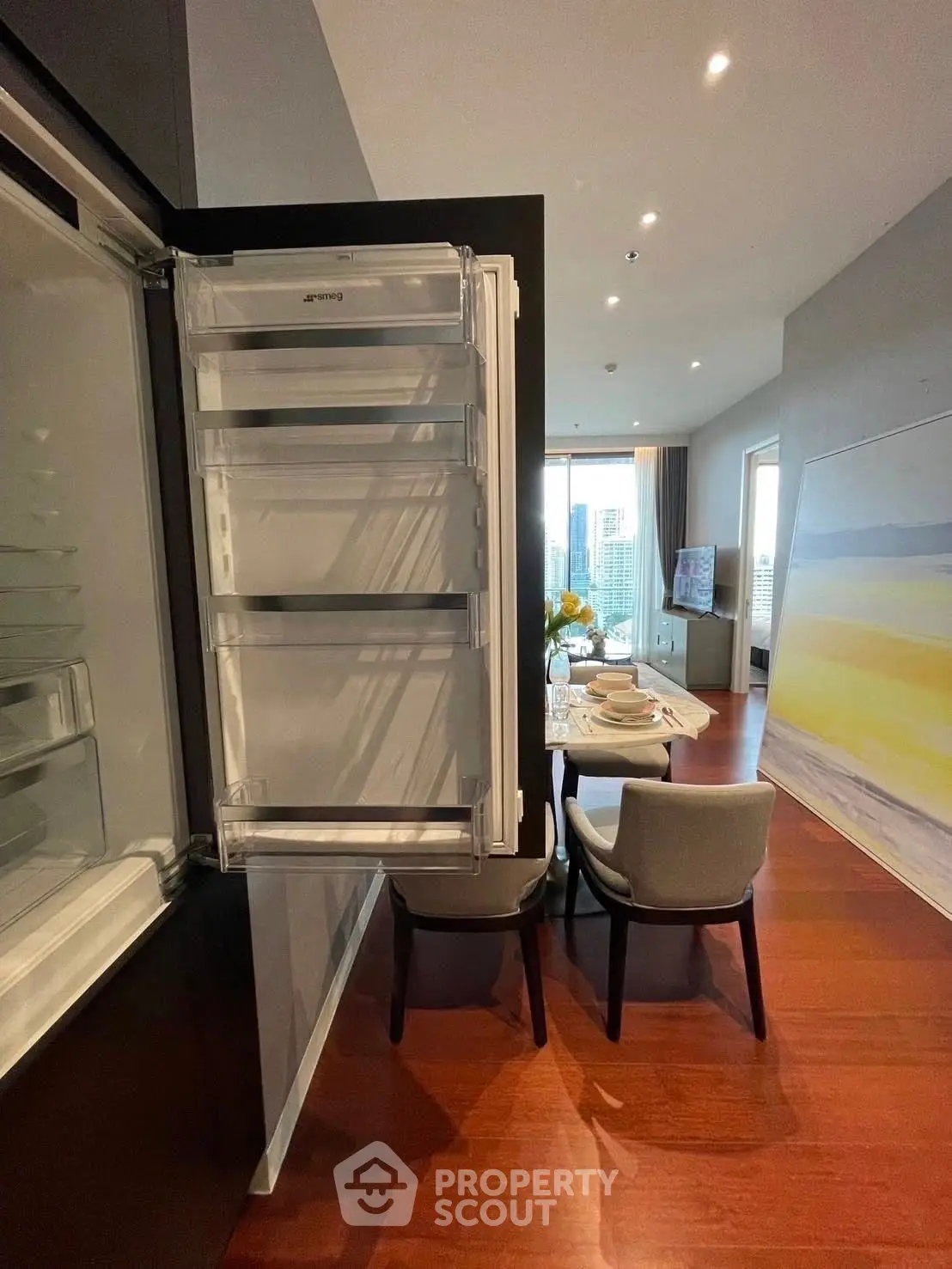 Modern dining area with open fridge and city view, perfect for urban living.