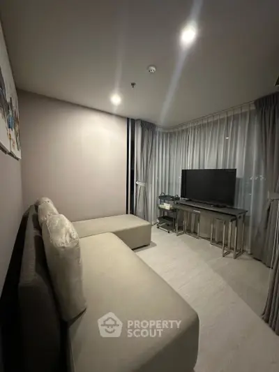 Modern living room with sleek design and cozy seating area, featuring a large TV and elegant curtains.