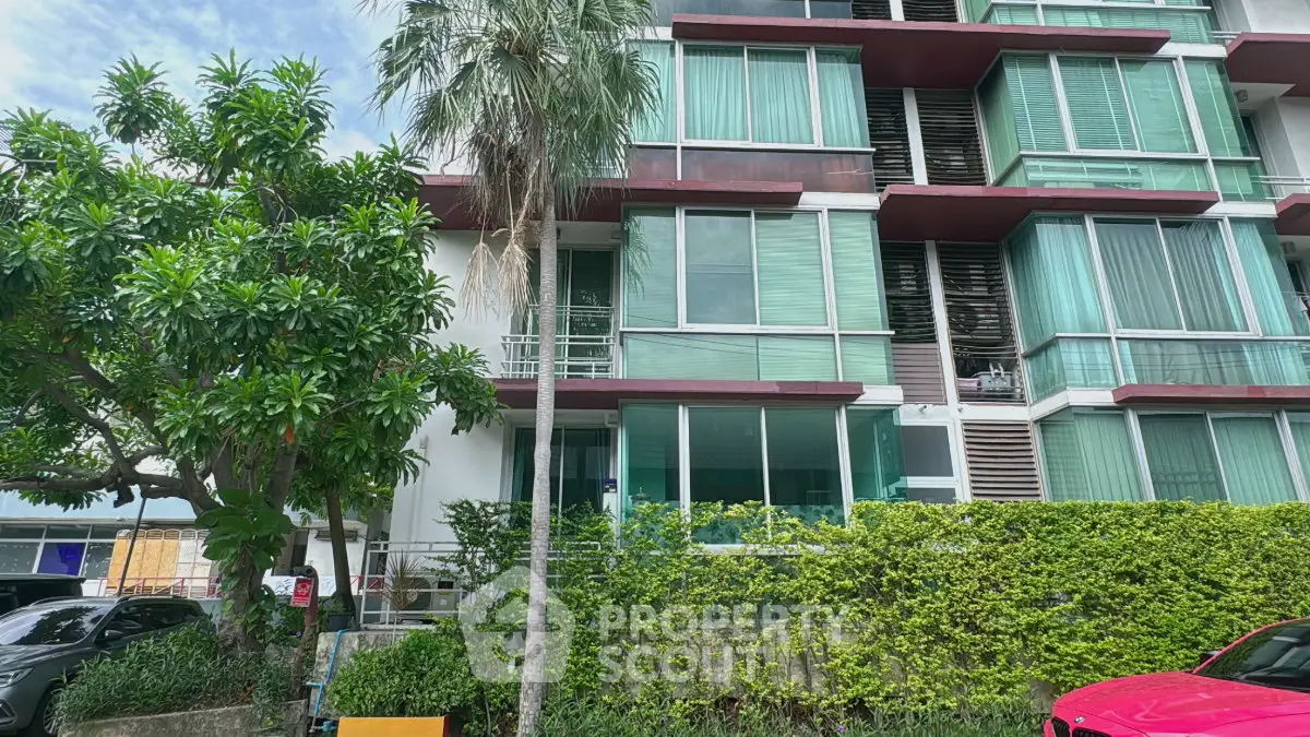 Modern apartment building with lush greenery and large windows in urban setting.