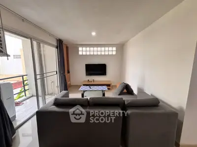 Spacious living room with modern sofa and wall-mounted TV, adjacent to a balcony with sliding glass doors.