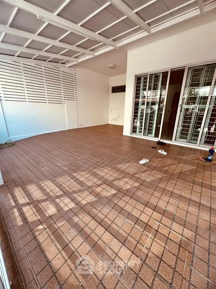 Spacious tiled patio with sliding glass doors and white lattice roof, perfect for outdoor relaxation.