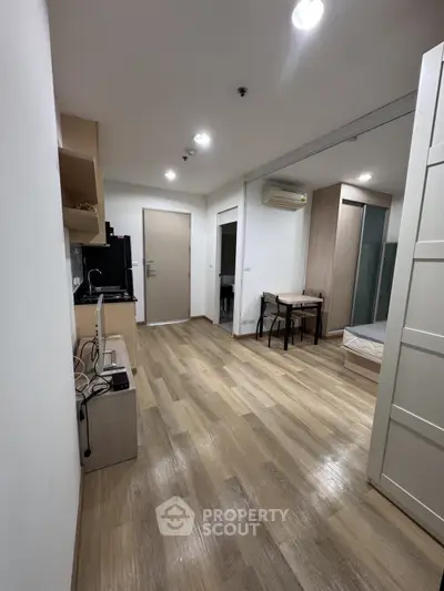 Modern studio apartment with wooden flooring and compact kitchen in open layout.