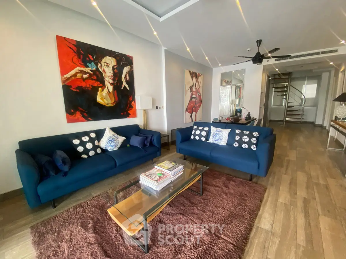Stylish living room with modern decor and vibrant artwork, featuring cozy blue sofas and a chic glass coffee table.