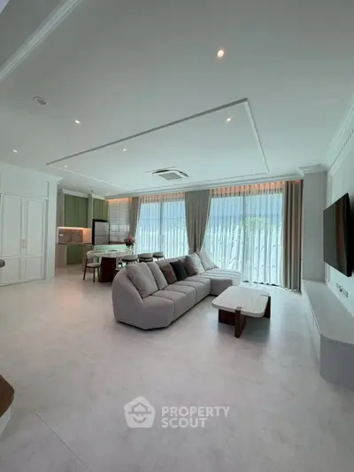 Spacious modern living room with open kitchen and large windows offering natural light.