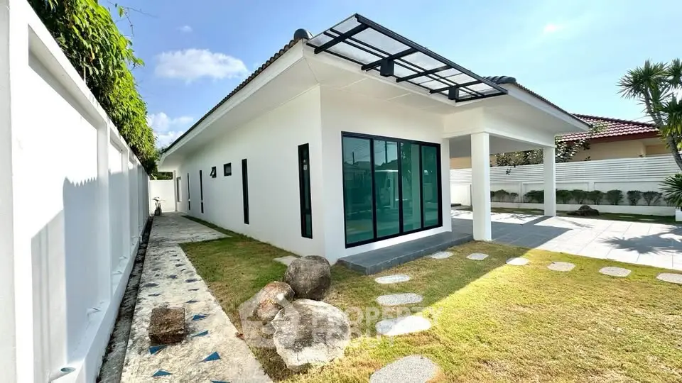 Modern single-story house with sleek design and spacious outdoor area, featuring large windows and a well-maintained lawn.