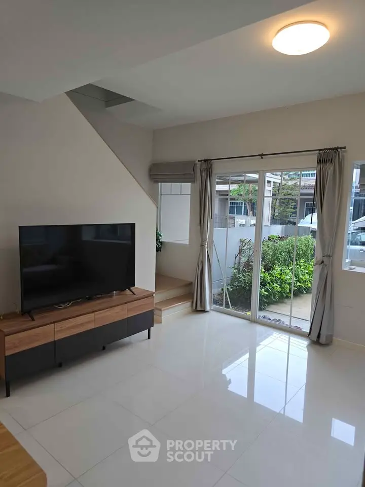 Modern living room with large TV and garden view through sliding glass doors.