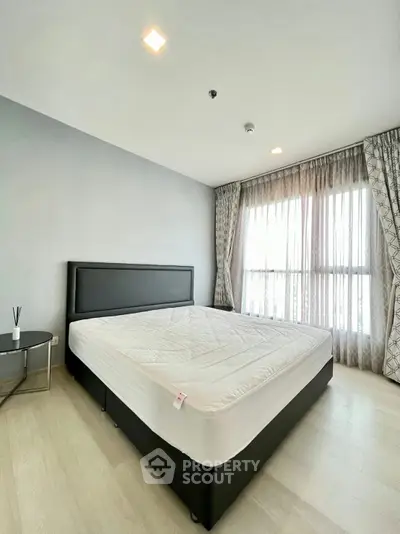 Spacious bedroom with large window and modern furnishings in a bright apartment.
