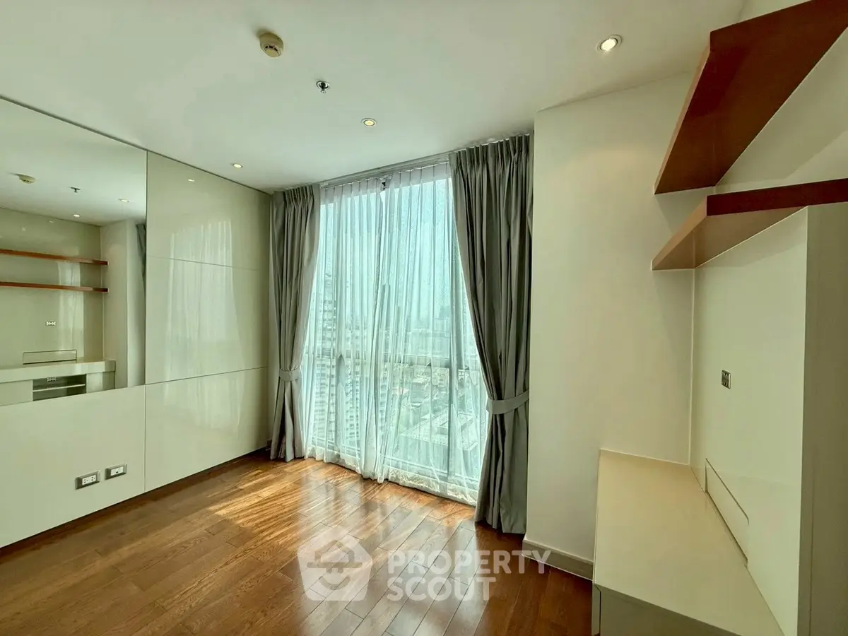 Spacious modern living room with large window and wooden flooring in high-rise apartment.