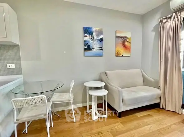 Cozy living room with modern decor, featuring a small sofa, glass dining table, and stylish wall art.