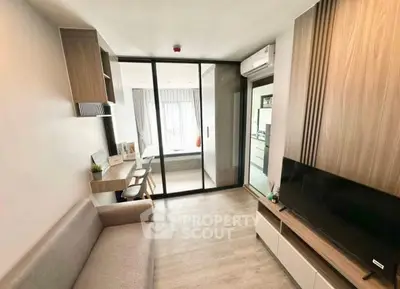 Modern living room with sleek design and glass partition leading to bedroom, featuring cozy sofa and wall-mounted TV.