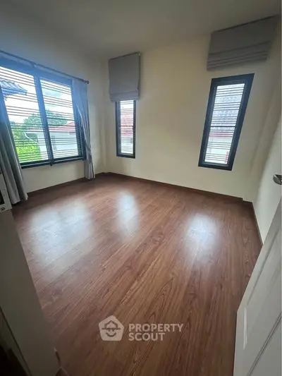 Spacious empty bedroom with wooden flooring and large windows for natural light.