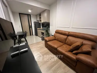 Modern living room with brown leather sofa and sleek kitchen area in open layout apartment.