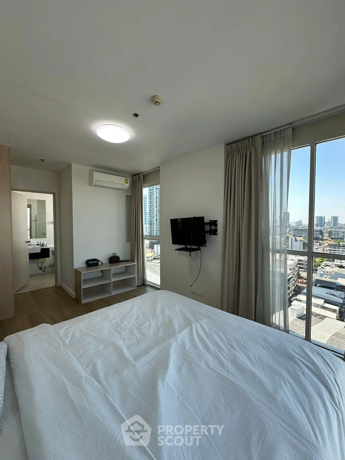 Modern bedroom with city view, featuring a wall-mounted TV and large windows.