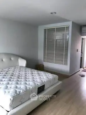 Spacious bedroom with modern design and large window blinds, perfect for relaxation.