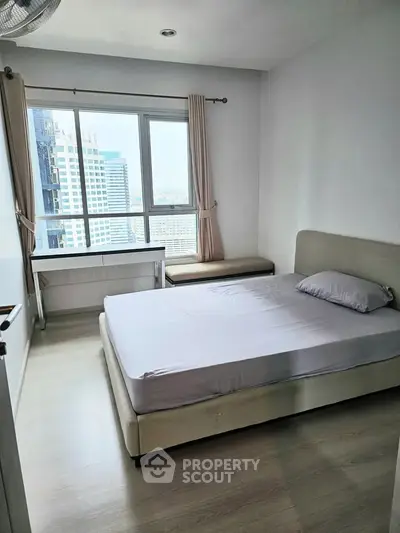 Modern bedroom with city view, featuring a comfortable bed and large window for natural light.