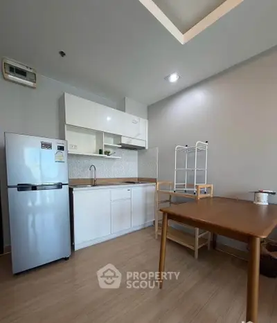 Modern kitchen with sleek white cabinets and compact fridge in a cozy apartment setting.